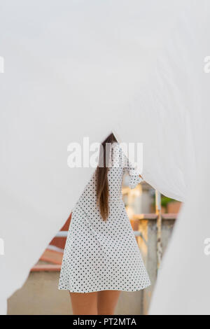 Back view of young woman standing behind drying bed sheet on roof terrace Stock Photo