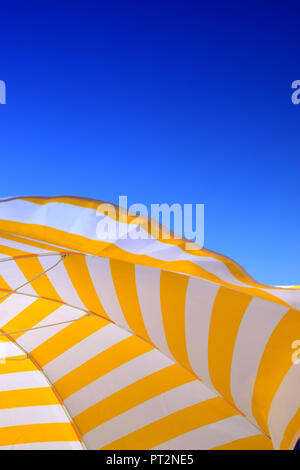 umbrella and blue sky background, yellow and white striped parasol in front of azure sky as a symbol of vacation Stock Photo