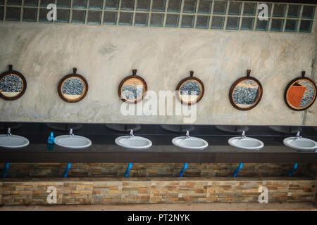 Row of white wash basins in the bathroom with row of mirrors in a public toilet. White clean ceramic sink bowls in the public men's toilet. Stock Photo