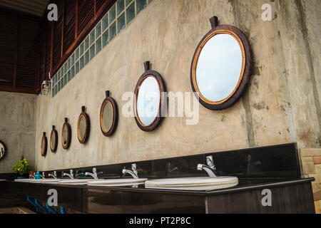 Row of white wash basins in the bathroom with row of mirrors in a public toilet. White clean ceramic sink bowls in the public men's toilet. Stock Photo