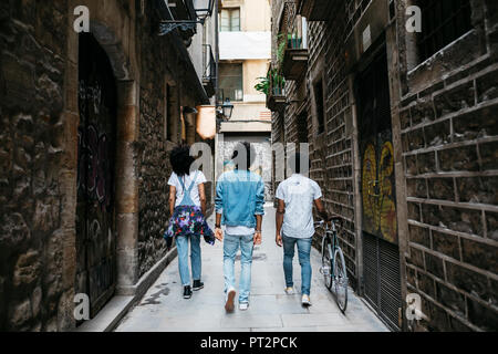 Spain, Barcelona, back view of three friends walking down an alley Stock Photo