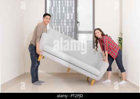Smiling couple carrying modern chair together placing furniture moving into new home, young family discussing house improvement interior design while  Stock Photo