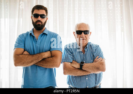 Portrait of adult grandson and his grandfather wearing sunglasses at home Stock Photo