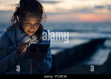 Woman using digital tablet on the beach at sunset Stock Photo