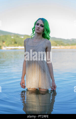 Portrait of young woman with dyed green hair standing dressed in water of lake Stock Photo