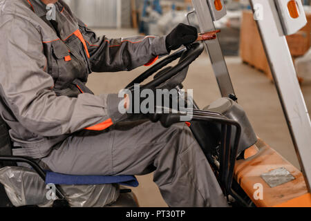 close - up steering wheel and levers. man driving a forklift through a warehouse in a factory. driver in uniform and protective helmet. the concept of logistics and storage Stock Photo