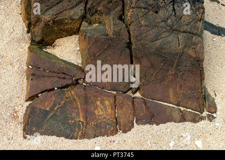 A Red geometrical stone formation on a beach, made up with broken triangles , square, rectangles,  missing one piece, and containing straight lines. Stock Photo