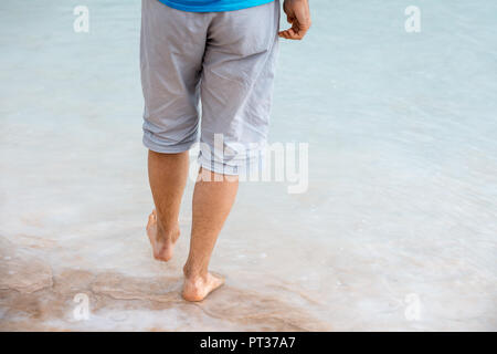 A man walks barefoot on the salty beach of the Dead Sea Stock Photo