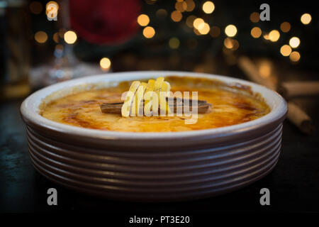 CREME BRULEE (CREAM BRULEE, BURNT CREAM) IN TERRACOTA CAZUELA DISHES ON OLD BAKING. SERVED WITH CANELLA AND LEMON DECORATION AND CHRISTMAS LIGHTS LIKE Stock Photo