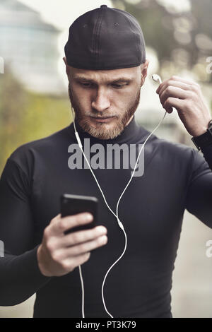 Close-up shot of young white man with beard putting headphone in his ear. Determined sportsman is ready for long-distance run and workout Athlete wear Stock Photo