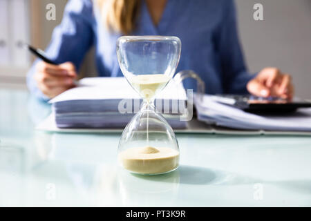 Close-up Of A Hourglass In Front Of Businesswoman Calculating Invoice Stock Photo