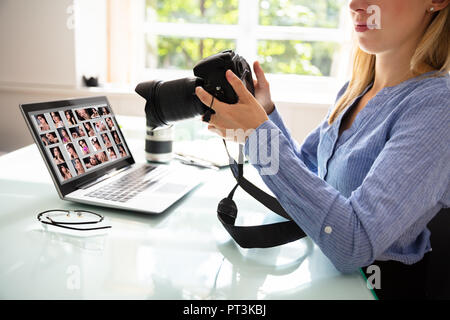 Female Editor Holding DSLR Camera With Laptop On Desk Stock Photo