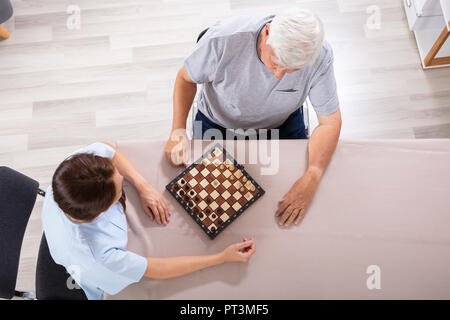 High Angle View Of Female Caretaker Playing Chess With Senior Man On Desk Stock Photo