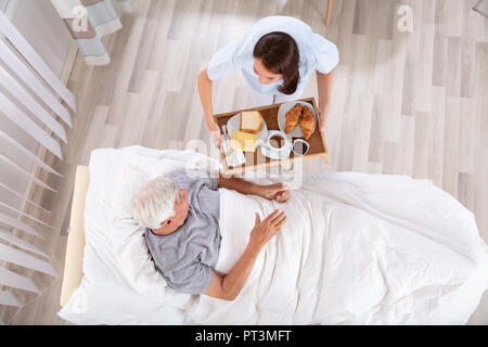 Overhead View Of Female Nurse Serving Food To Senior Male Patient In Clinic Stock Photo