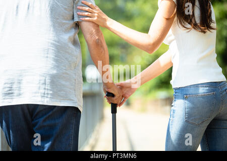 Close-up Of A Woman Assisting Her Father While Walking With Stick Stock Photo