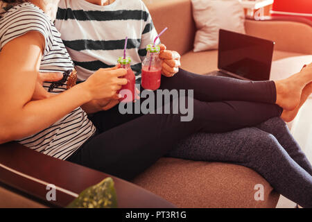 Couple in love drinking smoothie chilling on sofa in living room. Man and woman hugging while using laptop Stock Photo