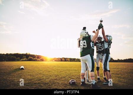 Ecstatic group of American football players standing in a huddle and celebrating with a trophy after a championship games Stock Photo