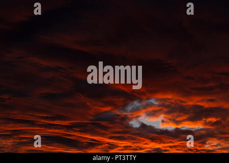 Clouds lit orange by sunset, gradient from darker to brighter. Cloud hole with blue sky. Stock Photo