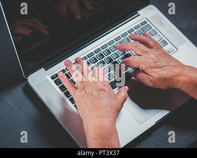 Grandmother works behind laptop, typing on keyboard with her old hands with wrinkles. Modern old pensioner working from home. Close up view of elderly Stock Photo