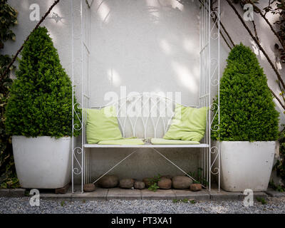 White garden bench made of iron with two green bushes in a flower pot on the side Stock Photo