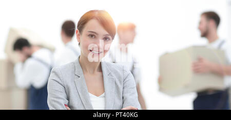 Smiling manager holding clipboard on blurred background with movers and boxes. Stock Photo