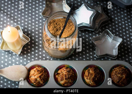 Aerial home baking themed composition with brown sugar, muffins in pan, star shaped molds and a glowing candle. Stock Photo