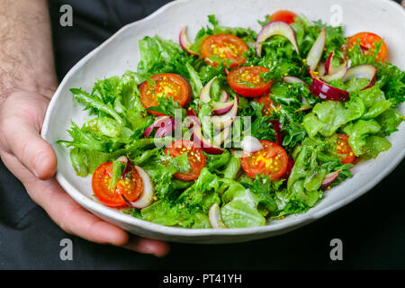 White plate with lettuce, cherry tomatoes and red onion salad with olive oil, mustard and wine vinegar dressing in men's hands. Delicious light dinner Stock Photo