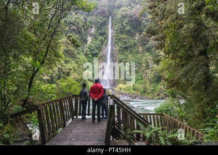 Tourists under the rain admiring Thunder Creek Falls, Mount Aspiring National Park, West Coast region, South Island, New Zealand, Stock Photo