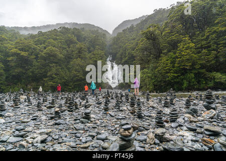 Tourists walking through rock cairns at Fantail Falls on a rainy day, Mount Aspiring National Park, West Coast region, South Island, New Zealand, Stock Photo