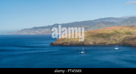 Boat sailing on the Atlantic Ocean at Point of St Lawrence, with the village of Canical in the background, Machico district, Madeira region, Portugal, Stock Photo