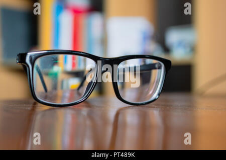 Eyeglasses on a table with bookshelf on background Stock Photo