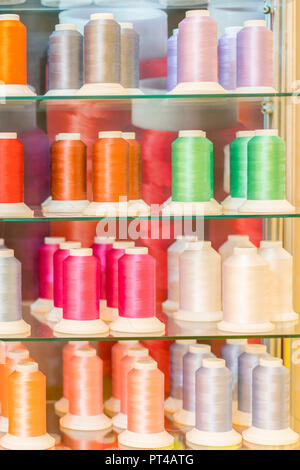 Background with a lot of colorful coils with threads. Bobbins are stacked in three rows, one on the other. The winding is erratic. Multicolored thread Stock Photo