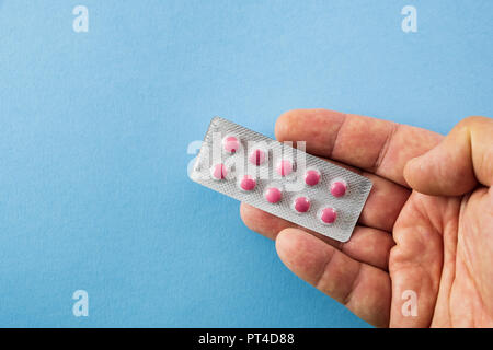 Diagonally arranged hand holding a blister pack of pink pills on blue background with copyspace- healthcare and medical concept Stock Photo