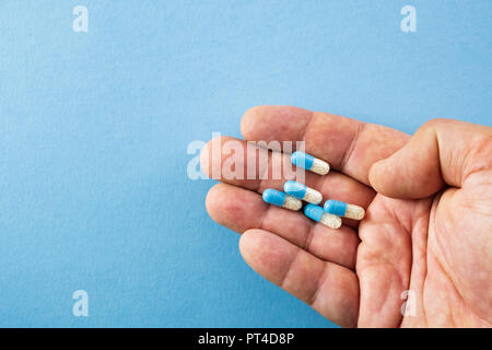 Diagonally arranged hand holding blue and white pills on blue background with copyspace- healthcare and medical concept Stock Photo