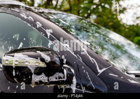 Black dirty car in white soap foam at car wash service station