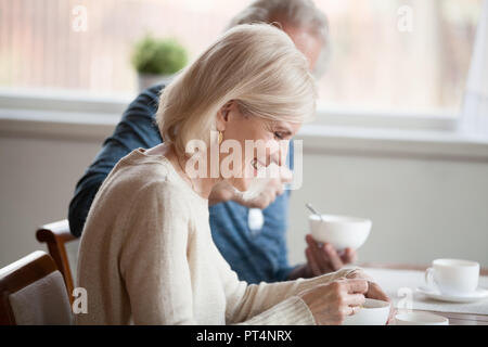 Happy grey haired woman having breakfast with aged husband at home, smiling beautiful old lady enjoys morning meal with mature man, senior family coup Stock Photo