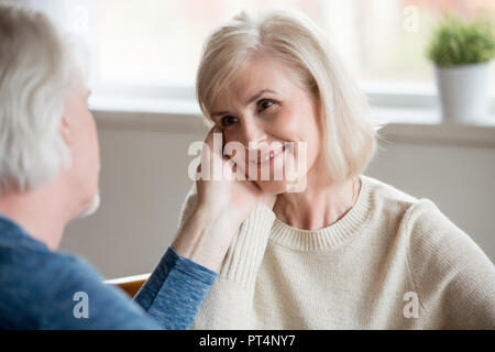 Caring senior husband touching beautiful face of smiling middle aged happy wife looking at husband with love devotion, old family couple enjoying tend Stock Photo