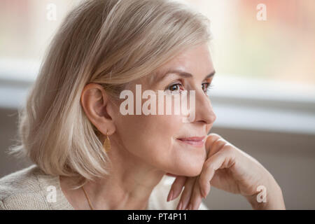 Dreamy thoughtful mature attractive woman relaxing hoping thinking of happy future, smiling senior middle aged lady looking away realizing positive th Stock Photo