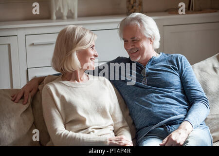 Happy loving senior couple talking looking in eyes relaxing on sofa together, elderly middle aged family embracing having fun enjoying conversation at Stock Photo