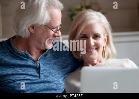 Loving senior husband in glasses looking at smiling middle aged wife using laptop together, happy mature couple enjoying spending time with computer a Stock Photo