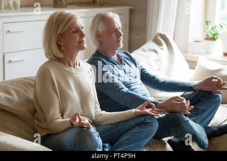 Senior couple meditating practicing yoga together sitting at hom Stock Photo