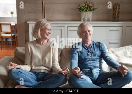 Old couple having fun laughing doing yoga together at home Stock Photo