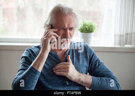 Stressed senior man having heart attack while talking on phone Stock Photo
