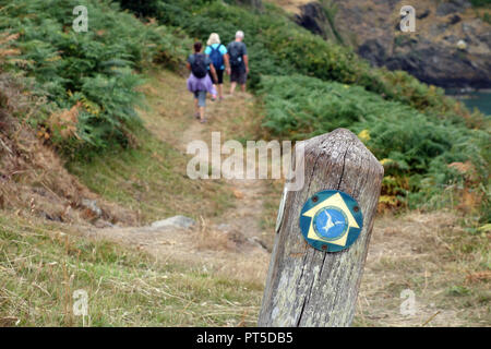 A Man & Two Women Hikers Walking by a Wooden Signpost on the Isle of Anglesey Coastal Path, Wales, UK. Stock Photo