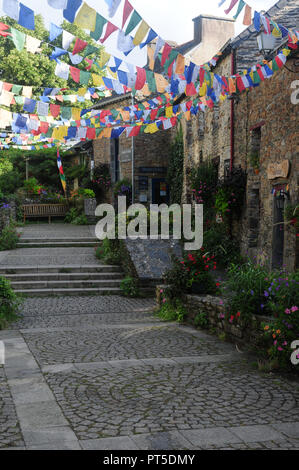 Cobbled street in the village of La Gacilly, Brittany, France with strings of Buddhist prayer flags hanging outside a Tibetan shop. Stock Photo