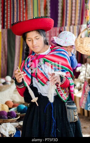 Chinchero, Peru - Sep 15, 2016: A young woman in traditional clothing explains the knitting process which includes the dyeing of alpaca and sheep wool Stock Photo