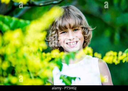 Portrait of young boy with yellow flowers in foreground, smiling. Stock Photo
