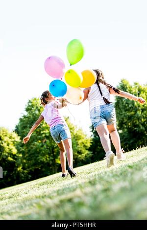 Girls running with balloons in park, smiling. Stock Photo
