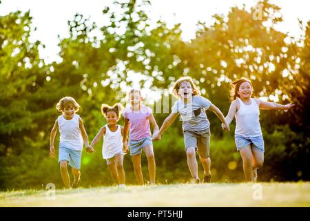 Children holding hands and running in park, laughing. Stock Photo