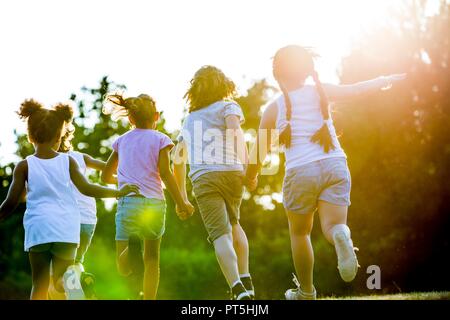 Children holding hands and running in park. Stock Photo